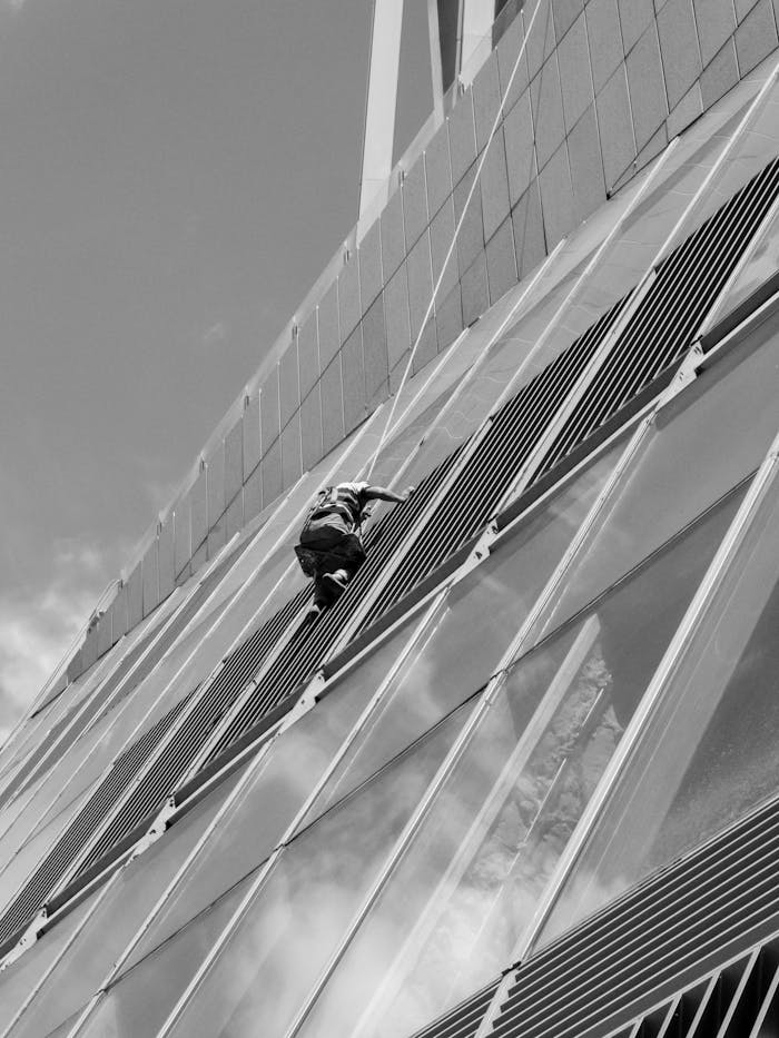 Black and white photo of a window cleaner working on a modern skyscraper facade, showcasing urban architecture.