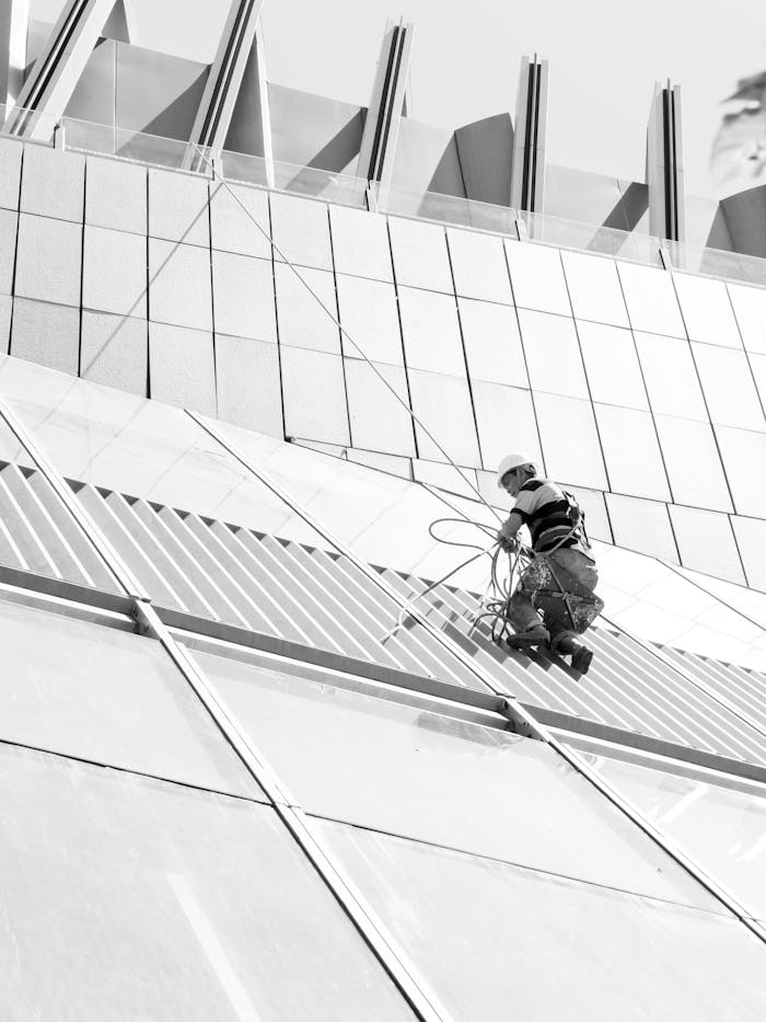 A professional window cleaner working on a contemporary glass building facade with a safety harness.